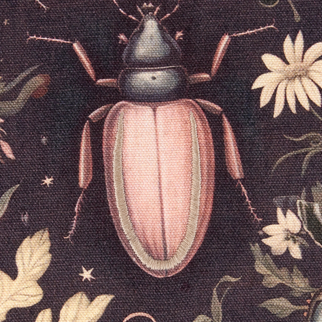 Embroidered pink beetle on a dark fabric background with floral patterns