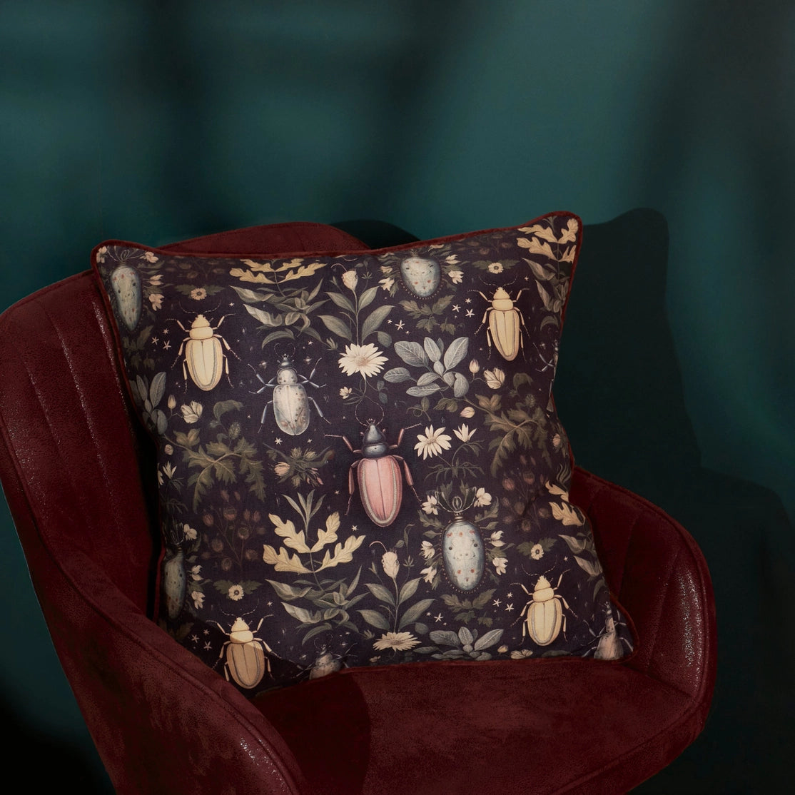 Decorative pillow with beetle and floral pattern on a dark background, placed on a red chair.