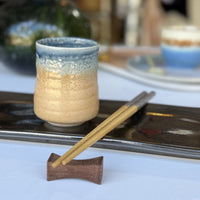 Ceramic cup with blue interior and beige exterior on a tray with chopsticks and wooden holder.