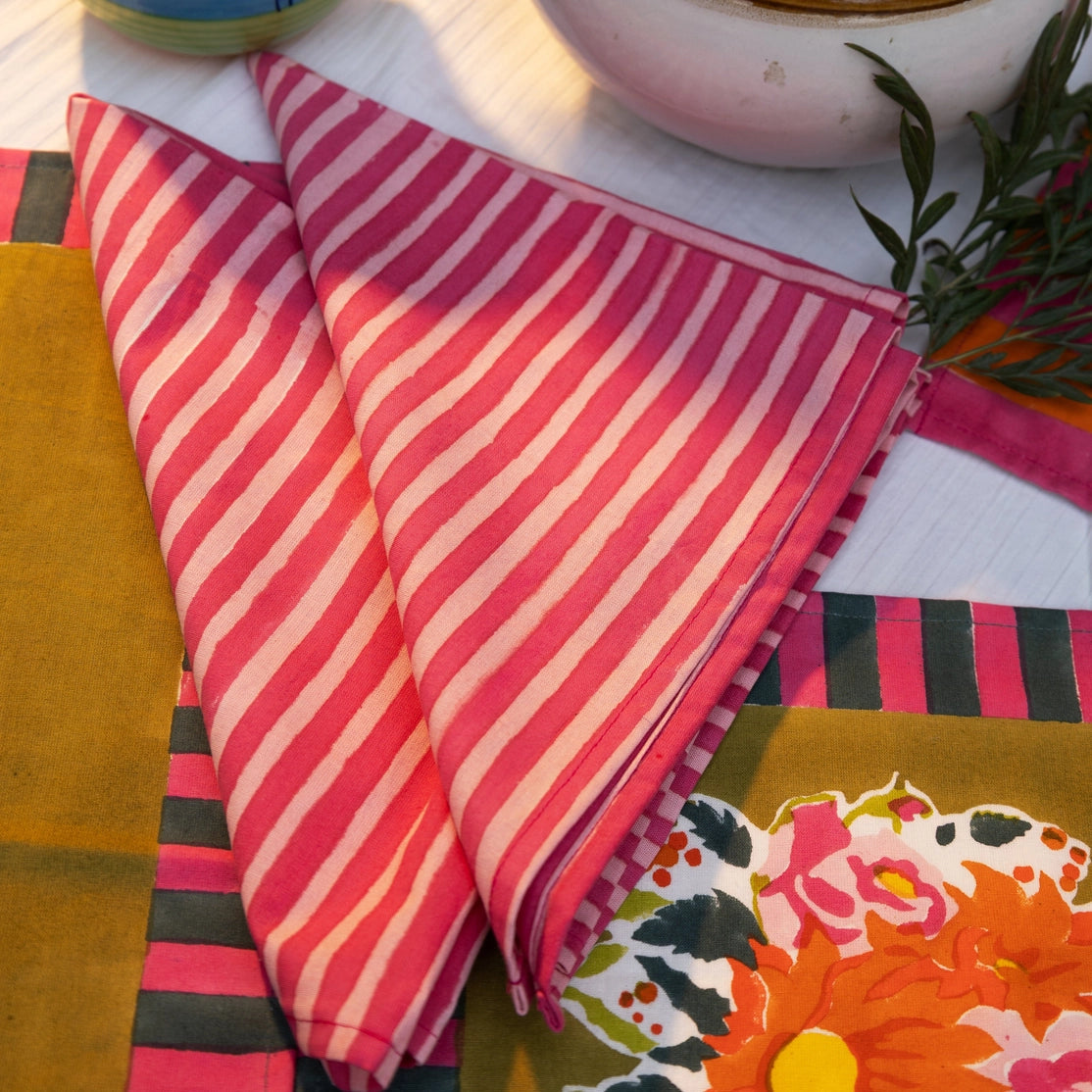 Pink and white striped fabric on a table with colorful bowls and floral tablecloth.