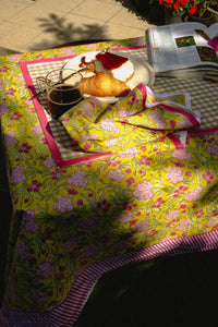 Table with a floral tablecloth, coffee, croissant, and magazine on a sunny outdoor patio.