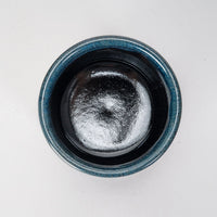 Blue and black ceramic container with a black interior on a white background