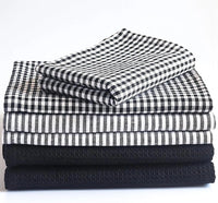 Stack of folded black and white checkered, striped, and textured towels on a white background