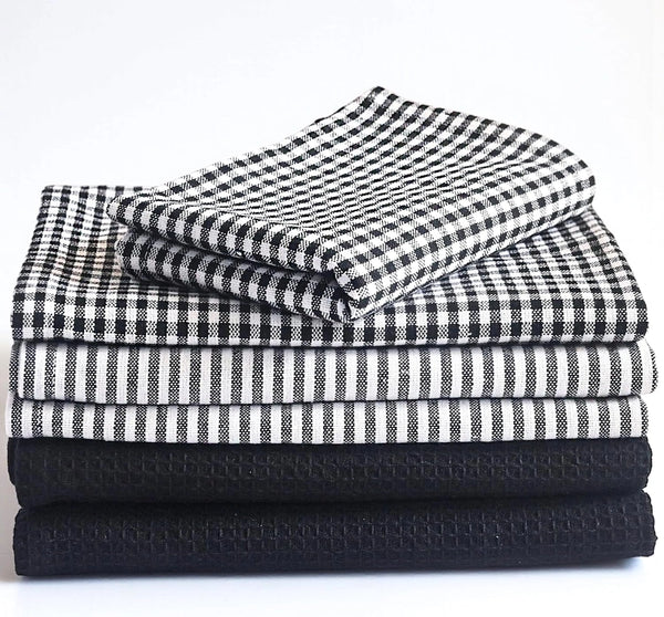 Stack of folded black and white checkered, striped, and textured towels on a white background