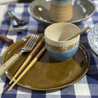 Ceramic cup with chopsticks on a plate with cutlery, on a checkered tablecloth.
