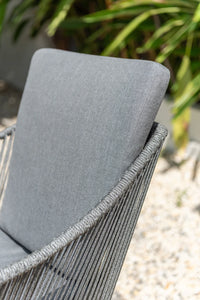 Gray cushioned chair with rope frame against a blurred natural background