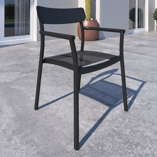 Black outdoor chair on a concrete patio with a building and plants in the background