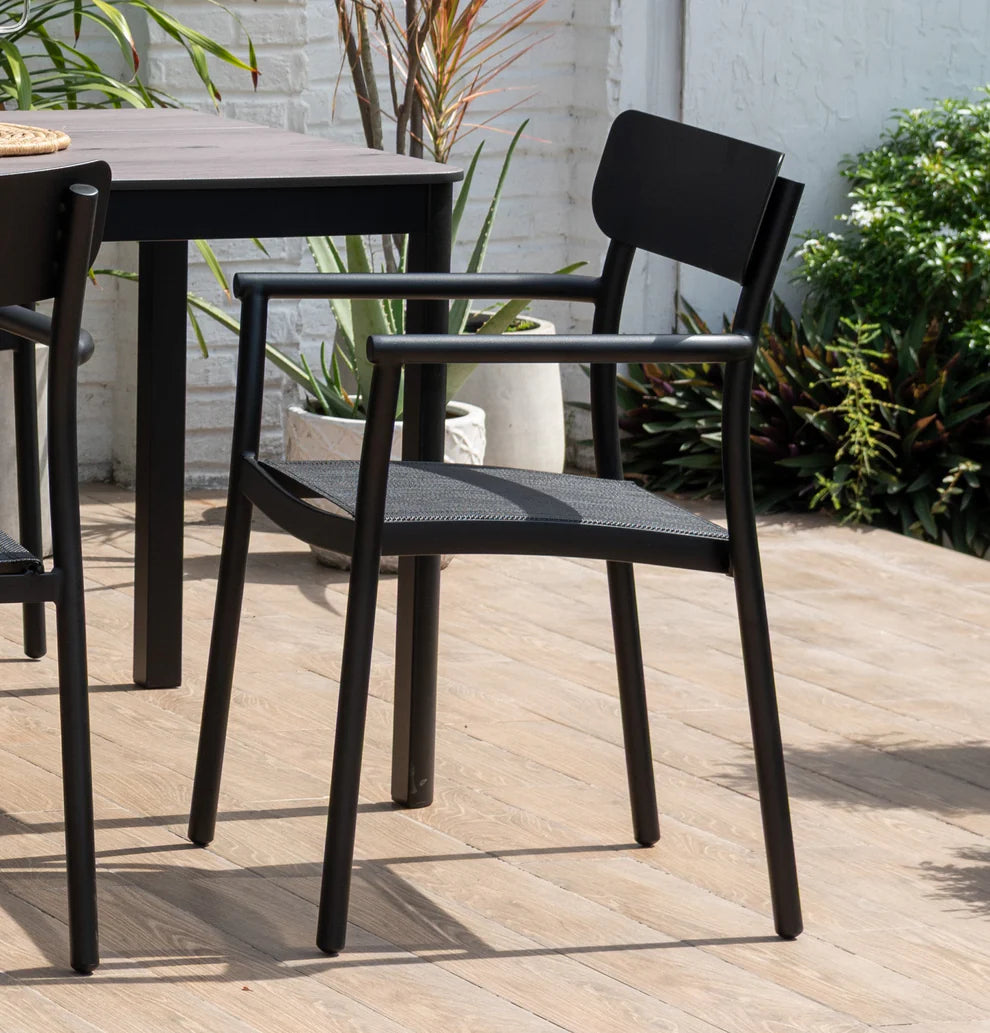 Black outdoor chairs and table on a wooden deck with plants in the background