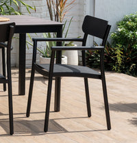 Black outdoor chairs and table on a wooden deck with plants in the background