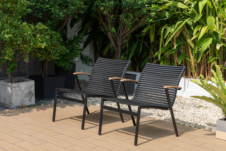 Two black outdoor chairs on a wooden deck with greenery in the background