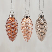 Three pine cone-shaped ornaments with textured surfaces on a light gray background