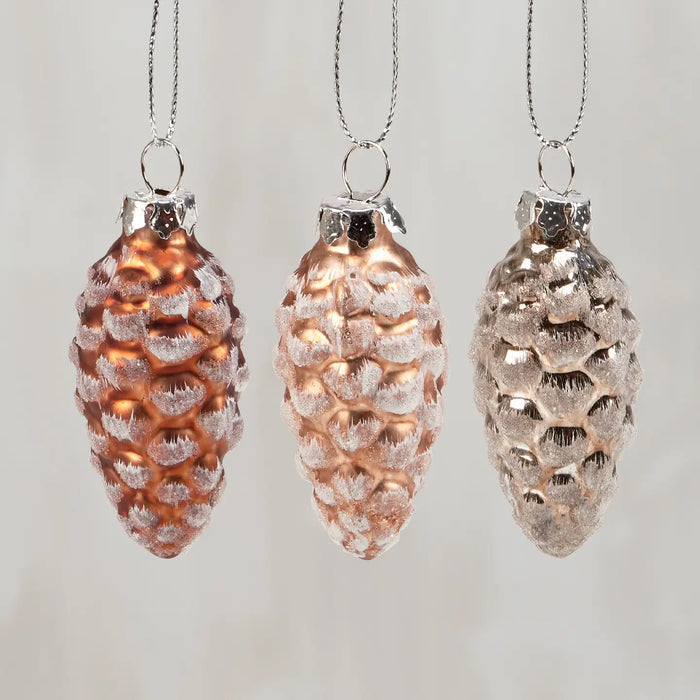 Three pine cone-shaped ornaments with textured surfaces on a light gray background
