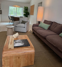 A modern living room featuring a dark brown fabric sofa with mint green pillows, a striped armchair, a wooden coffee table, and a tall floor lamp.