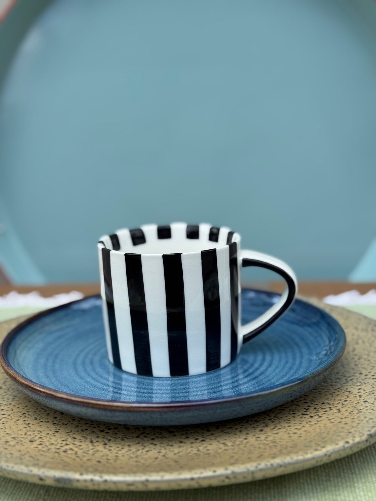 Black and white striped cup with blue saucer on a textured surface