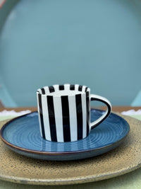 Black and white striped cup with blue saucer on a textured surface