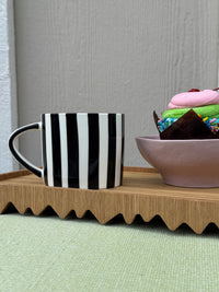 Black and white striped mug on a wooden tray with a colorful bowl in the background.