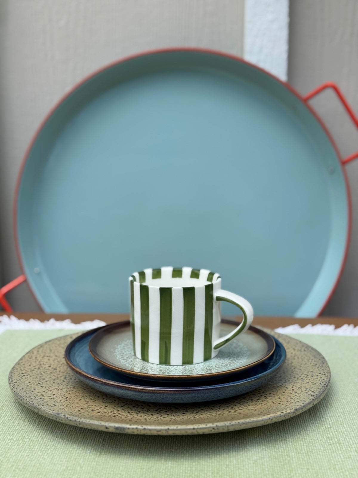 Set of ceramic plates and a striped mug on a green surface with a neutral background