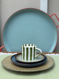 Set of ceramic plates and a striped mug on a green surface with a neutral background