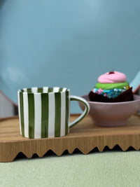 Green and white striped mug on a wooden tray with a cupcake in the background