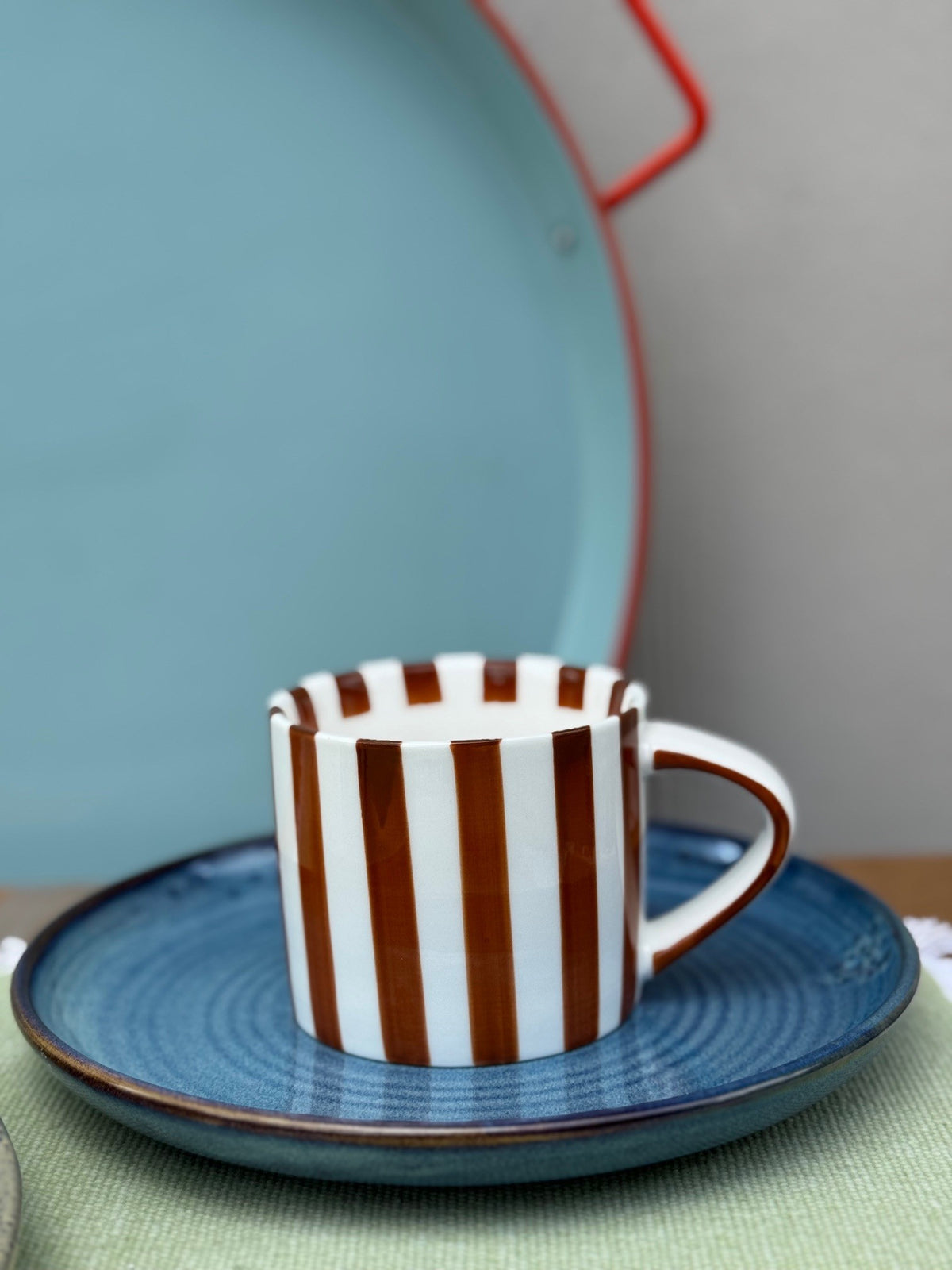 Striped ceramic cup and saucer on a blue plate with a light background