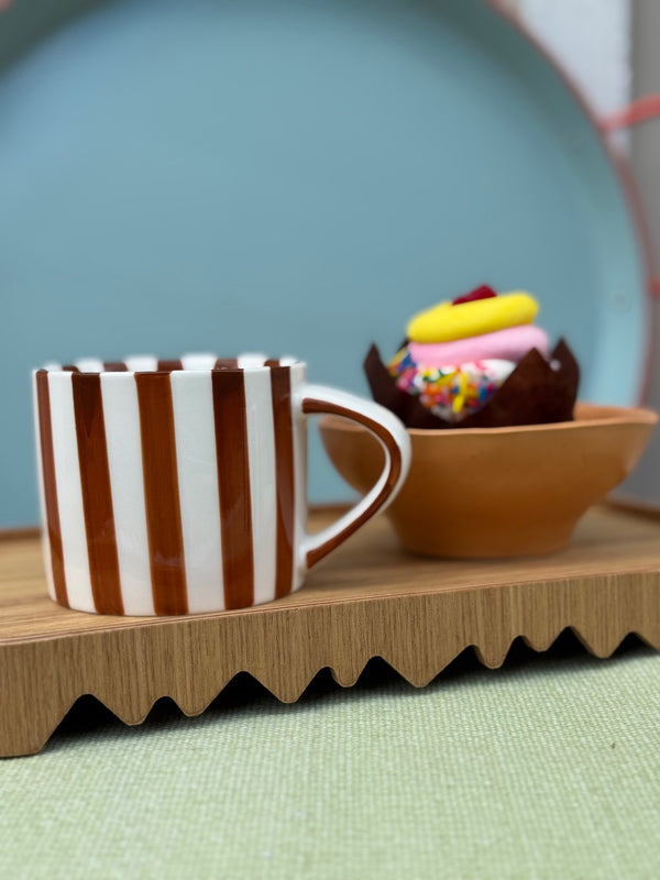 Striped mug on a wooden tray with a cupcake in the background