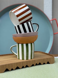 Stack of colorful striped mugs on a wooden tray with a blurred background