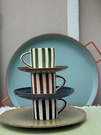 Stack of ceramic cups with striped patterns on a wooden surface.
