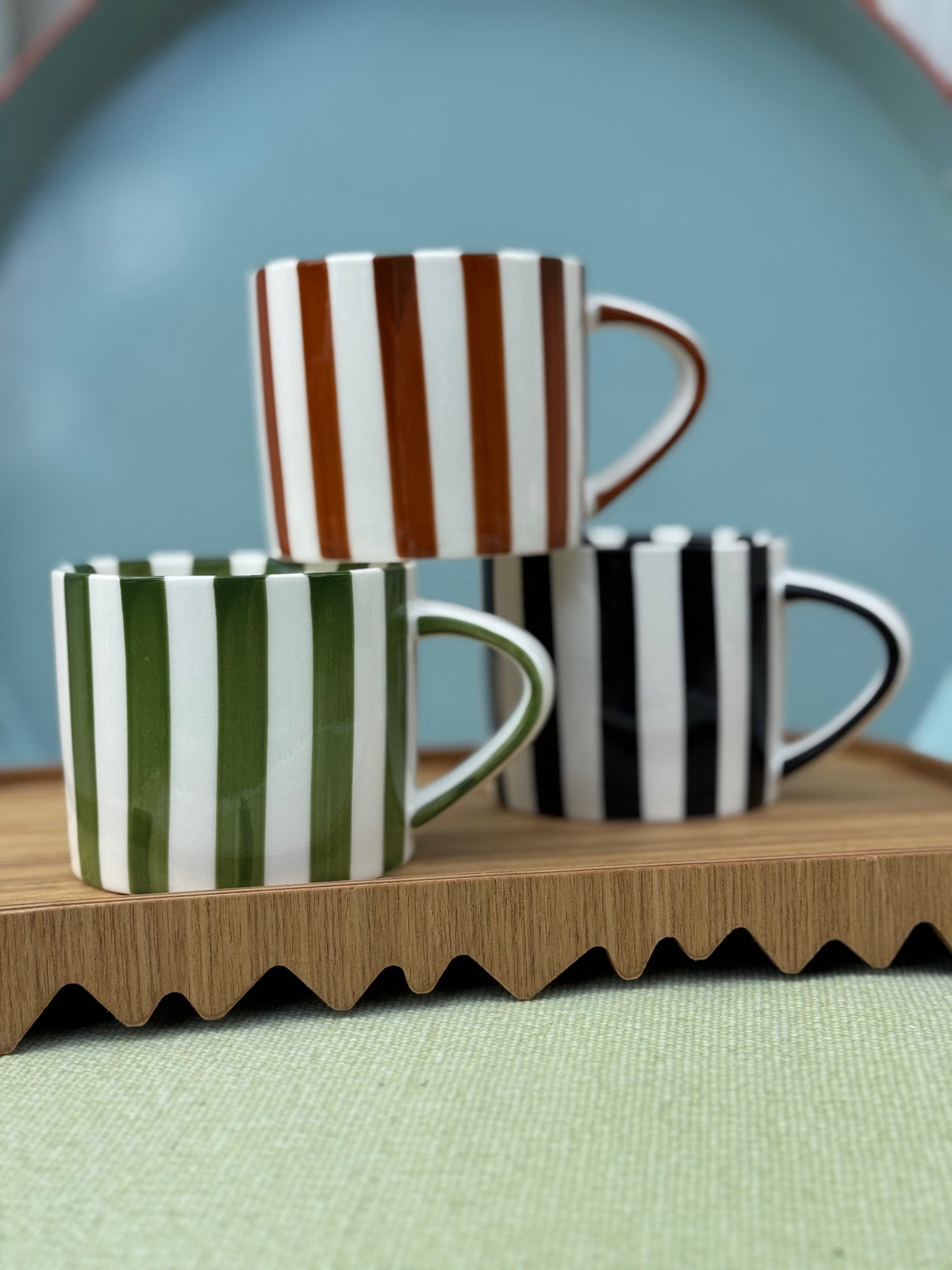 Three striped mugs on a wooden shelf with a blue wall background