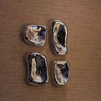 Four chrome wall sculptures on a brown textured surface