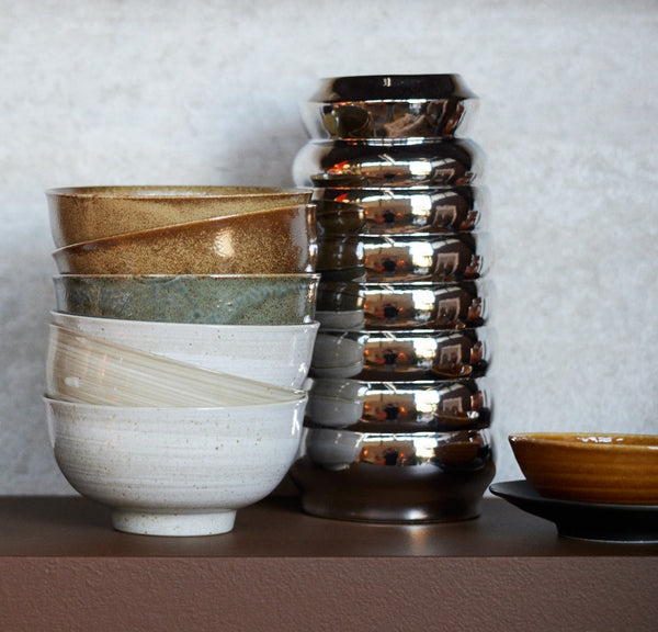 Set of ceramic bowls and a tall, reflective vase on a neutral background