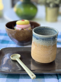 Ceramic cup with blue interior and beige exterior on a tray with a spoon, blurred background
