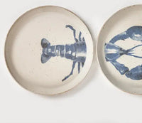 Two round speckled ceramic plates with blue lobster illustrations, shown on a clean white background.