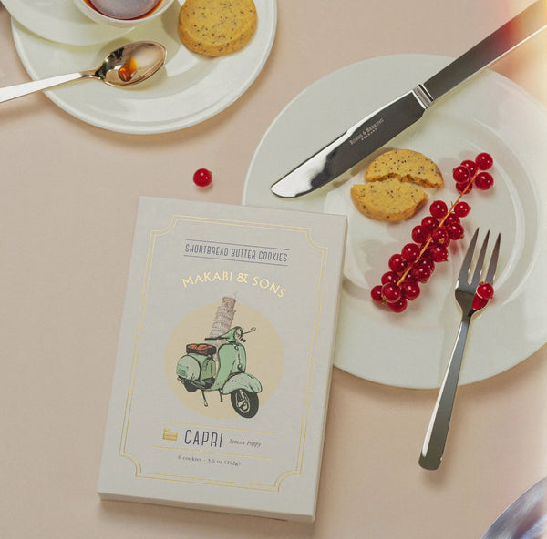 Book titled 'Capri' by Makabi & Sons on a table with cookies and red berries.