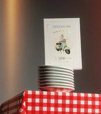 Stack of white cups with a branded paper product on top, placed on a red and white checkered tablecloth.