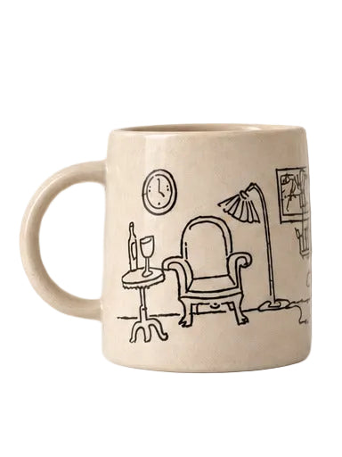 A cream-colored ceramic mug featuring a black line art illustration of a cozy living room scene with an armchair, side table, lamp, and clock.