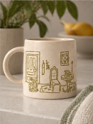 An off-white ceramic mug featuring a brown line-art illustration of a cozy room scene with a chair, table, and door.