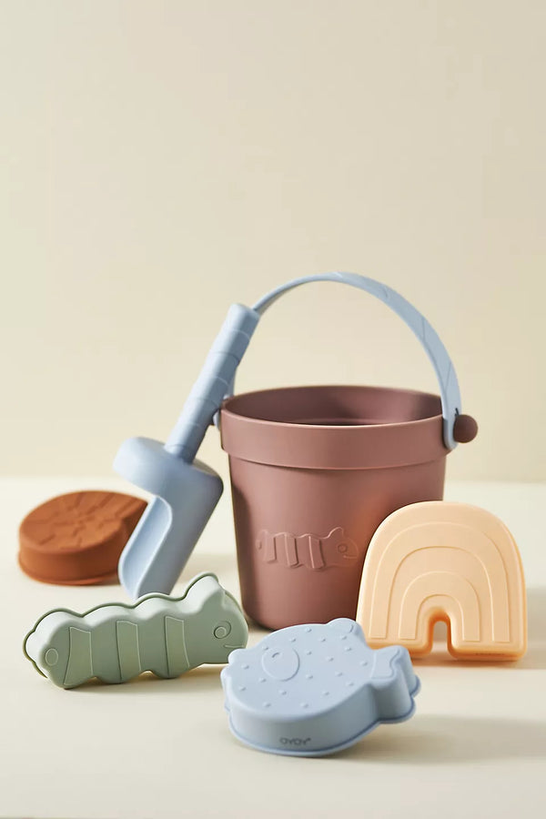 Set of colorful children's play items including a bucket, molds, and a shovel on a light background