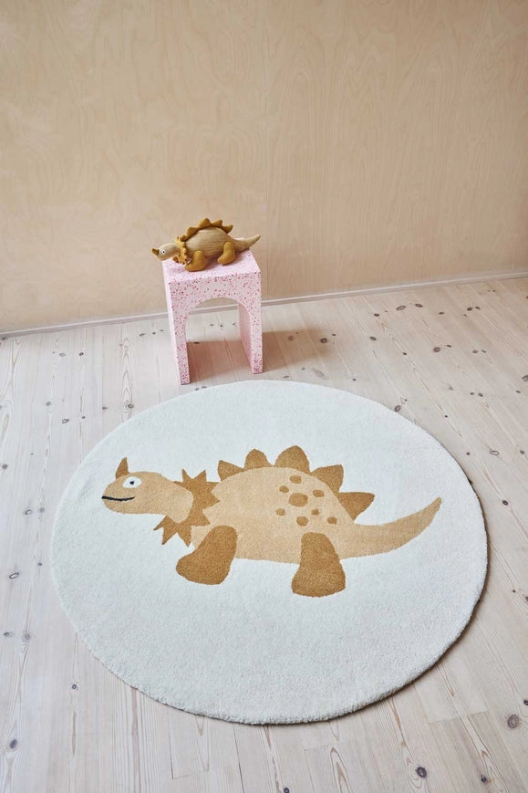 Round dinosaur rug on a wooden floor with a small pink stool and toy in the background.