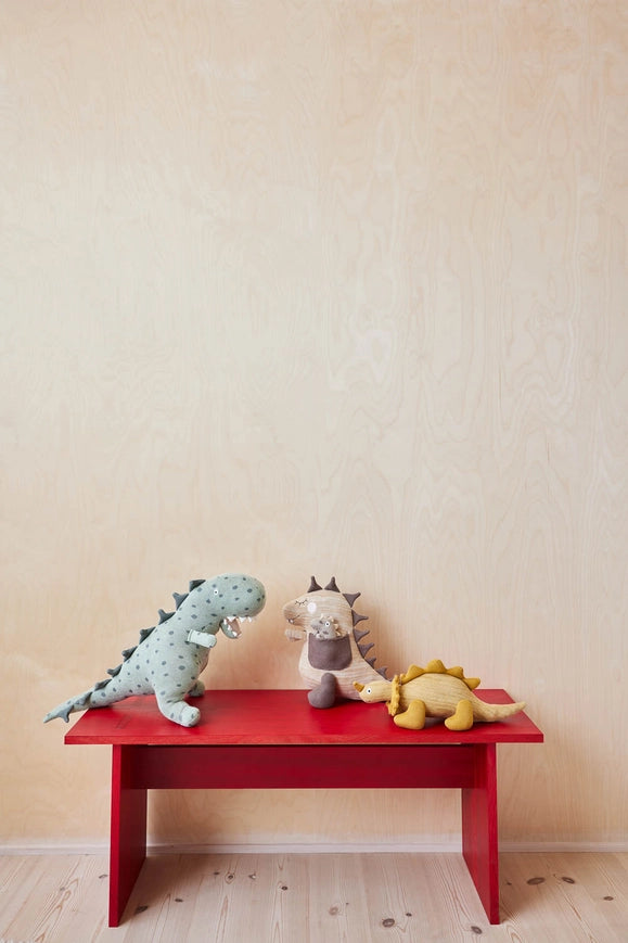 Three stuffed animals on a red bench against a beige wall.