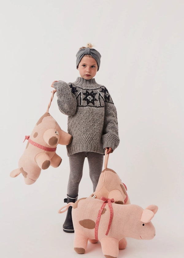 Child wearing a gray knit sweater with star pattern, holding two pink stuffed pigs against a white background