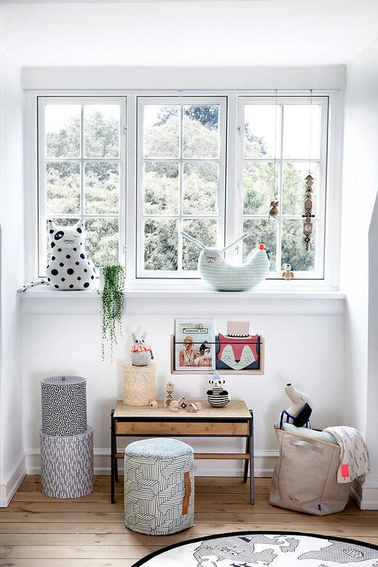 Children's room with a desk, chairs, and decorative items near a large window.