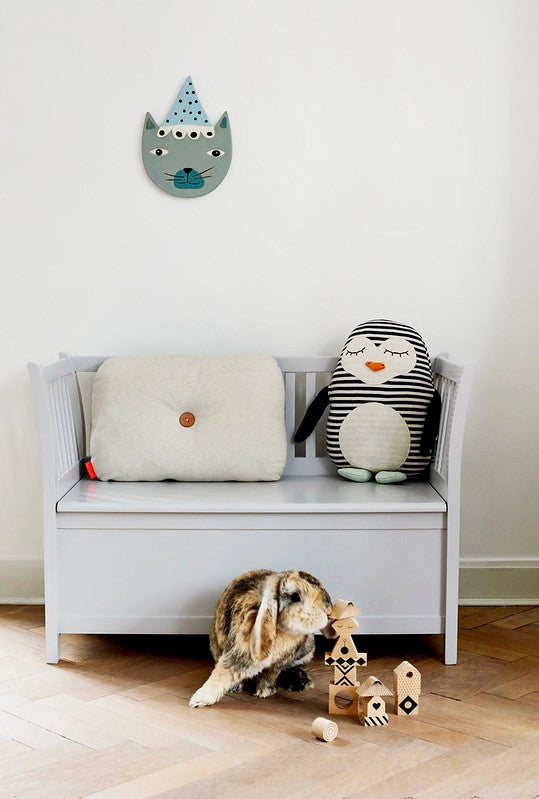 White bench with plush toys and a cat playing with wooden toys on a wooden floor.