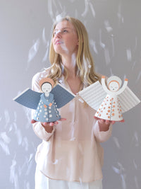 Woman holding two angel figurines against a light gray background