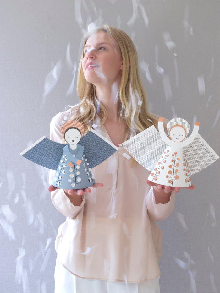 Woman holding two angel figurines against a light gray background