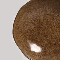 Close-up of a brown ceramic plate with reactive glaze on a light gray background