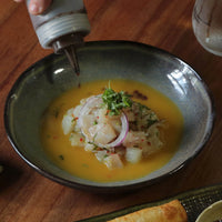 Dish with seafood and vegetables being drizzled with a sauce on a wooden table