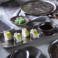 Sushi with kiwi slices on a black tray with soy sauce and wasabi.