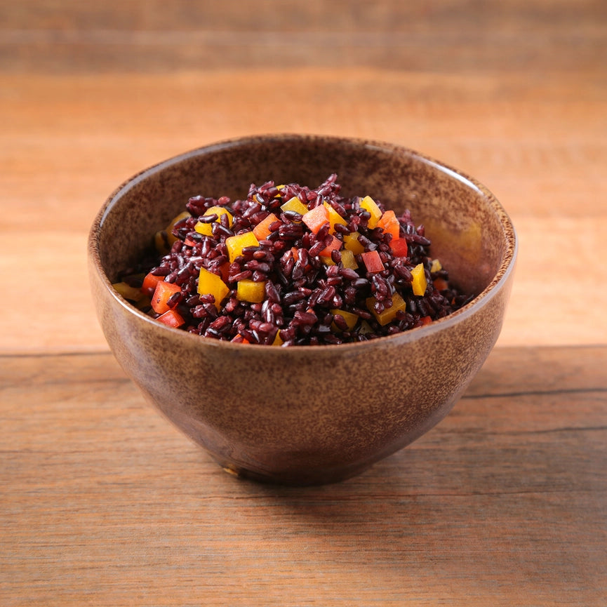 Brown bowl with black rice salad on a wooden surface