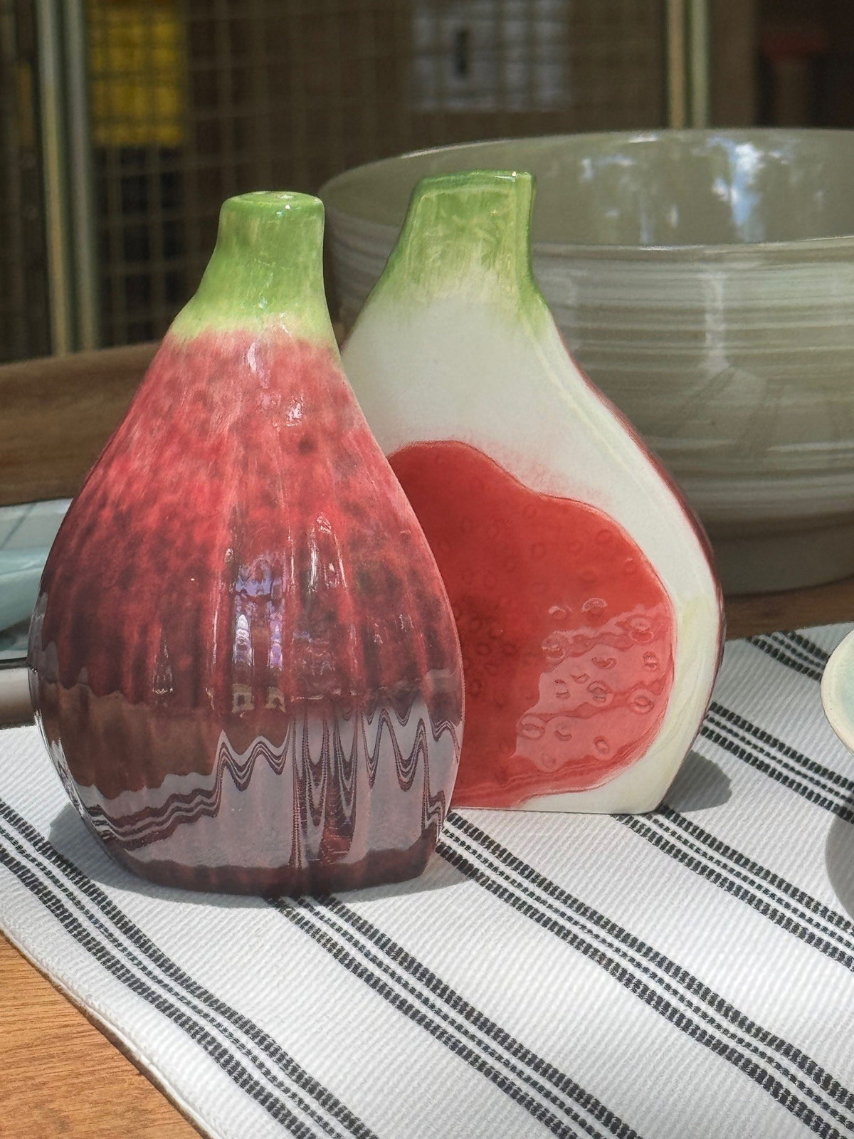 Two ceramic condiment shakers shaped like figs on a striped tablecloth.