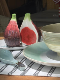 Decorative salt and pepper shakers shaped like figs on a table with a bowl and spoon.